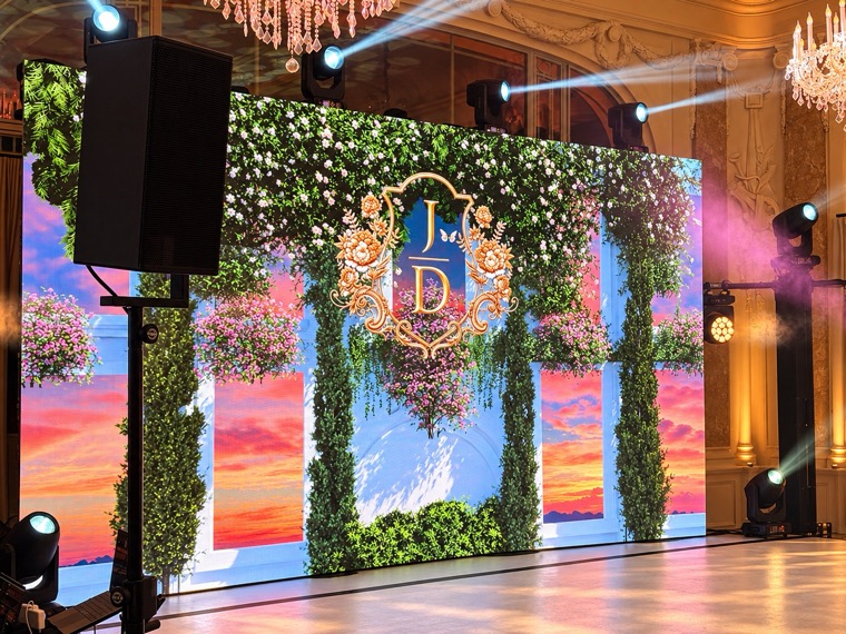 Mur de LED affichant un décor végétal fleuri avec monogramme doré, encadré de lyres et d’enceintes, dans un salon à lustres