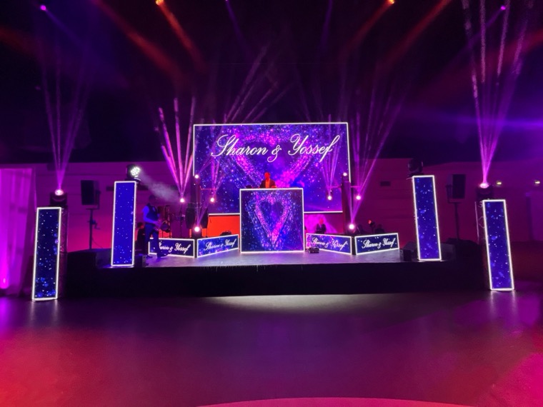 Scène avec mur de LED violet et cœur lumineux, colonnes LED et lyres, DJ et musiciens sur scène