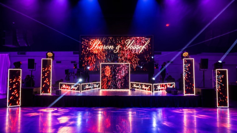 Scène de mariage avec mur de LED central, colonnes LED et façades lumineuses diffusant un feu d’artifice, faisceaux de lyres