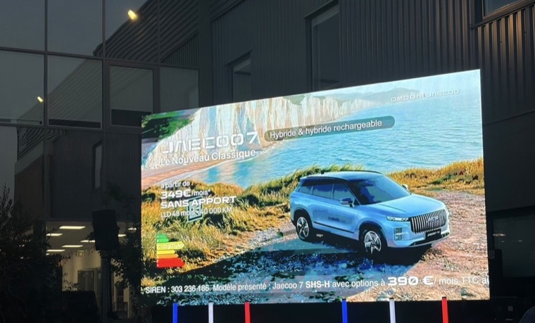 Mur de LED extérieur installé devant un bâtiment à la tombée de la nuit pendant la Coupe du monde, diffusant une publicité automobile, colonnes LED bleu, blanc, rouge au pied de l’écran